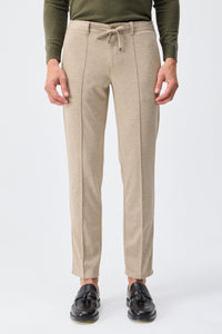 Herenbroek met trekkoord in taupe- of havermoutbeige kleur, getailleerde pasvorm en taps toelopende pasvorm.