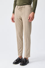 Herenbroek met trekkoord in taupe- of havermoutbeige kleur, getailleerde pasvorm en taps toelopende pasvorm.