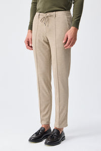 Herenbroek met trekkoord in taupe- of havermoutbeige kleur, getailleerde pasvorm en taps toelopende pasvorm.