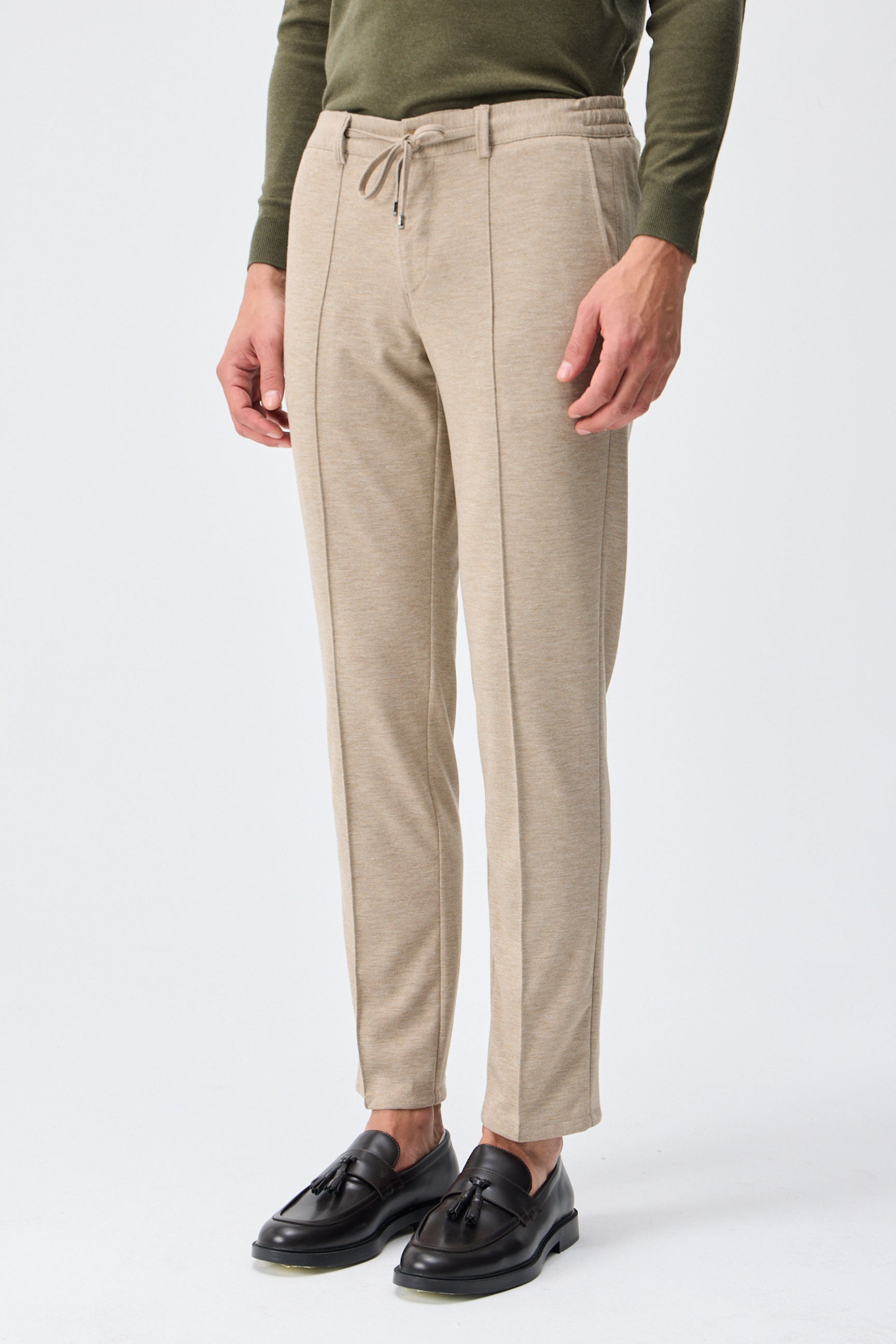 Herenbroek met trekkoord in taupe- of havermoutbeige kleur, getailleerde pasvorm en taps toelopende pasvorm.