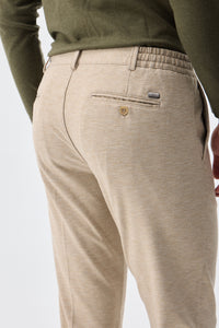 Herenbroek met trekkoord in taupe- of havermoutbeige kleur, getailleerde pasvorm en taps toelopende pasvorm.