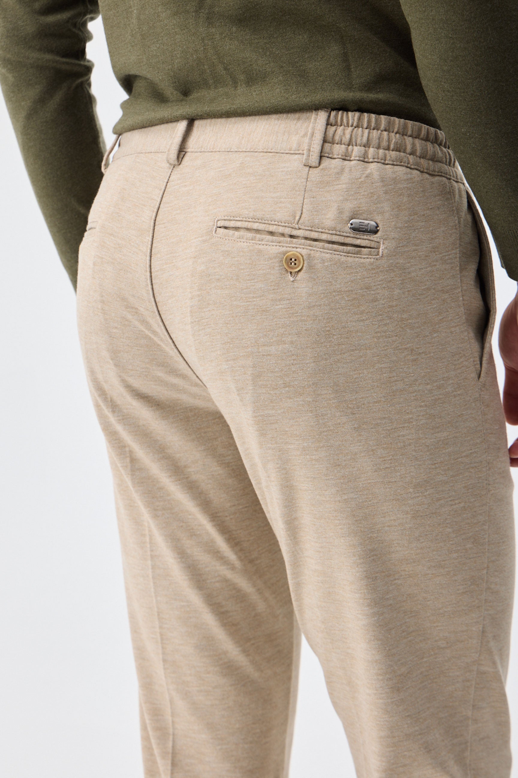 Herenbroek met trekkoord in taupe- of havermoutbeige kleur, getailleerde pasvorm en taps toelopende pasvorm.
